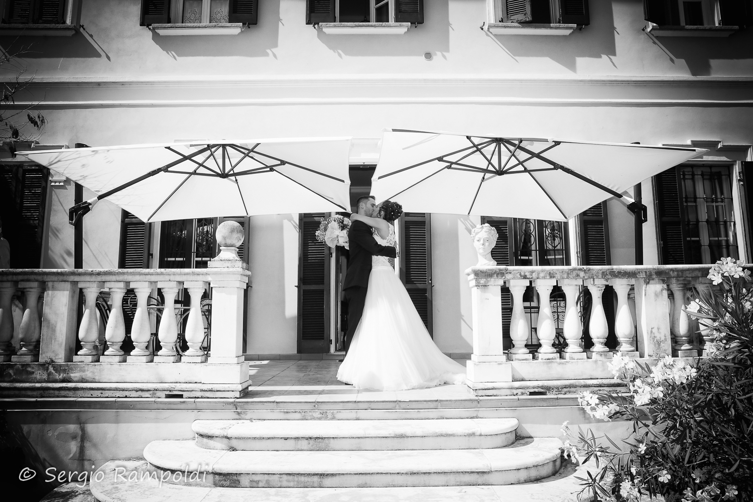 Una fotografia in bianco e nero dove gli Sposi abbracciati si baciano sulla veranda della villa